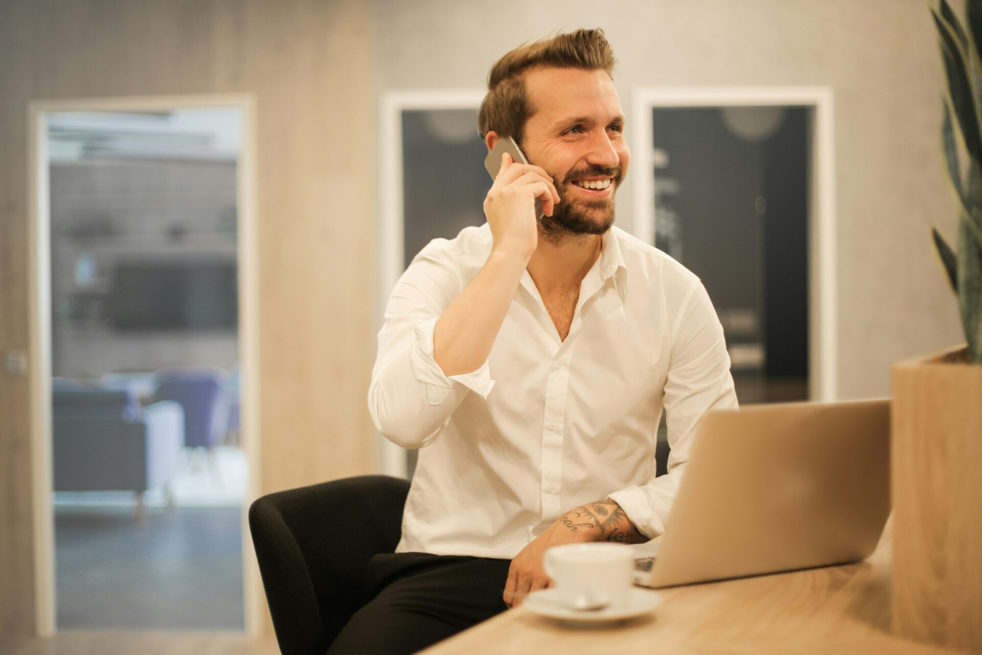 A man wearing a white shirt is talking on the phone, appearing engaged in a joyful conversation. This image relates to the concept of estate planning for business owners, highlighting the importance of planning and communication in managing business affairs and future assets.