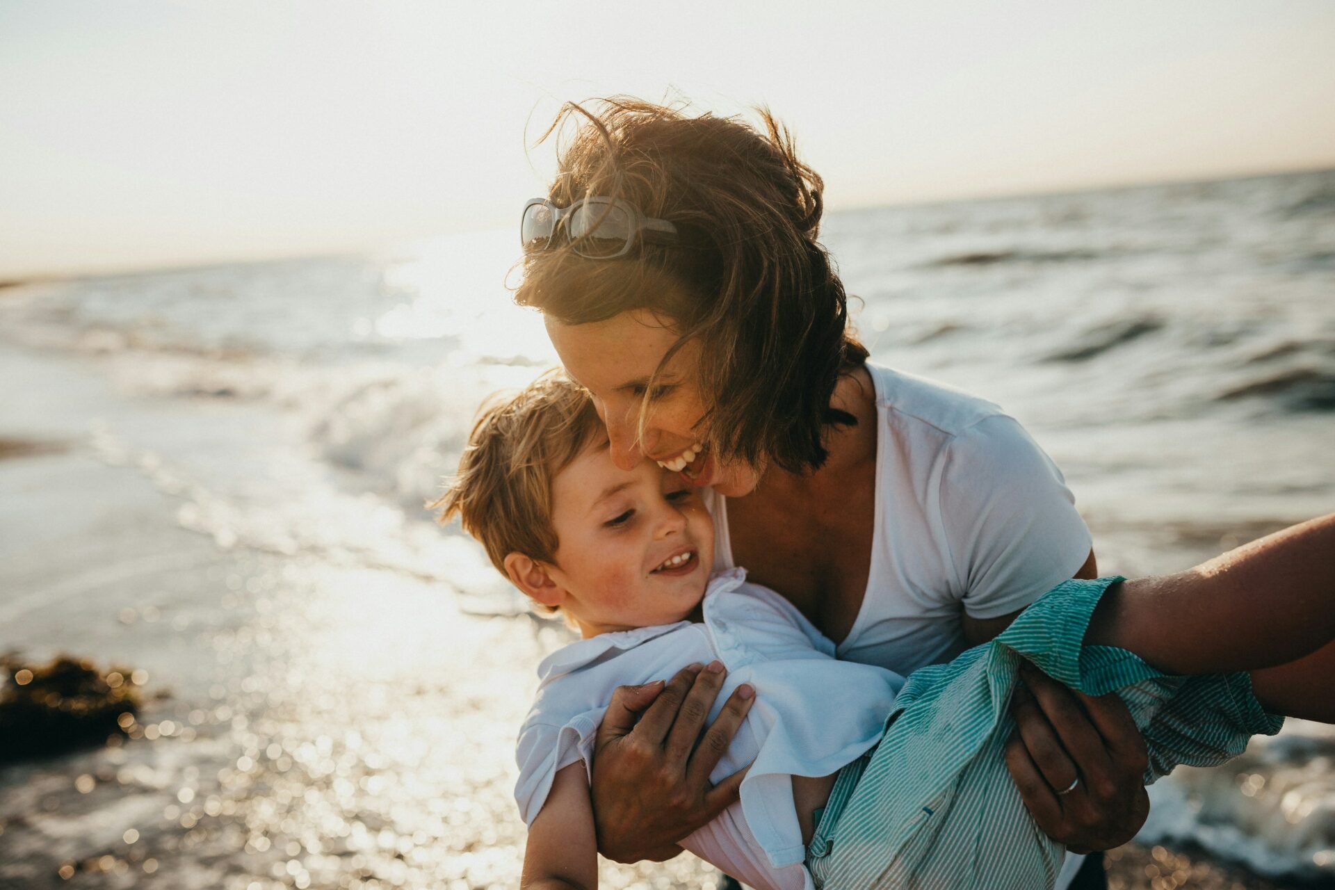 A mother and child are enjoying a sunny day on the beach, playing in the sand with the ocean in the background. This image represents the concept of life insurance in a trust, emphasizing the protection and security it offers for loved ones' future financial well-being.